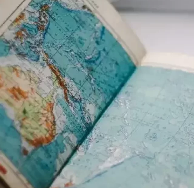 Livro aberto sobre uma mesa, nas duas páginas que estão a mostra está um mapa, onde maior parte representada é o mar.