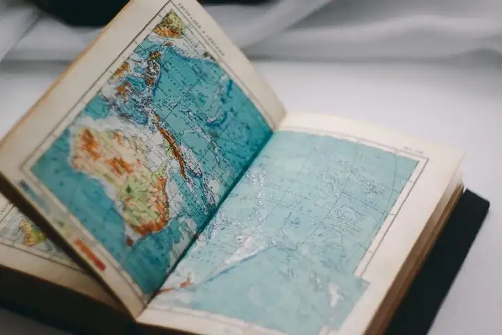 Livro aberto sobre uma mesa, nas duas páginas que estão a mostra está um mapa, onde maior parte representada é o mar.