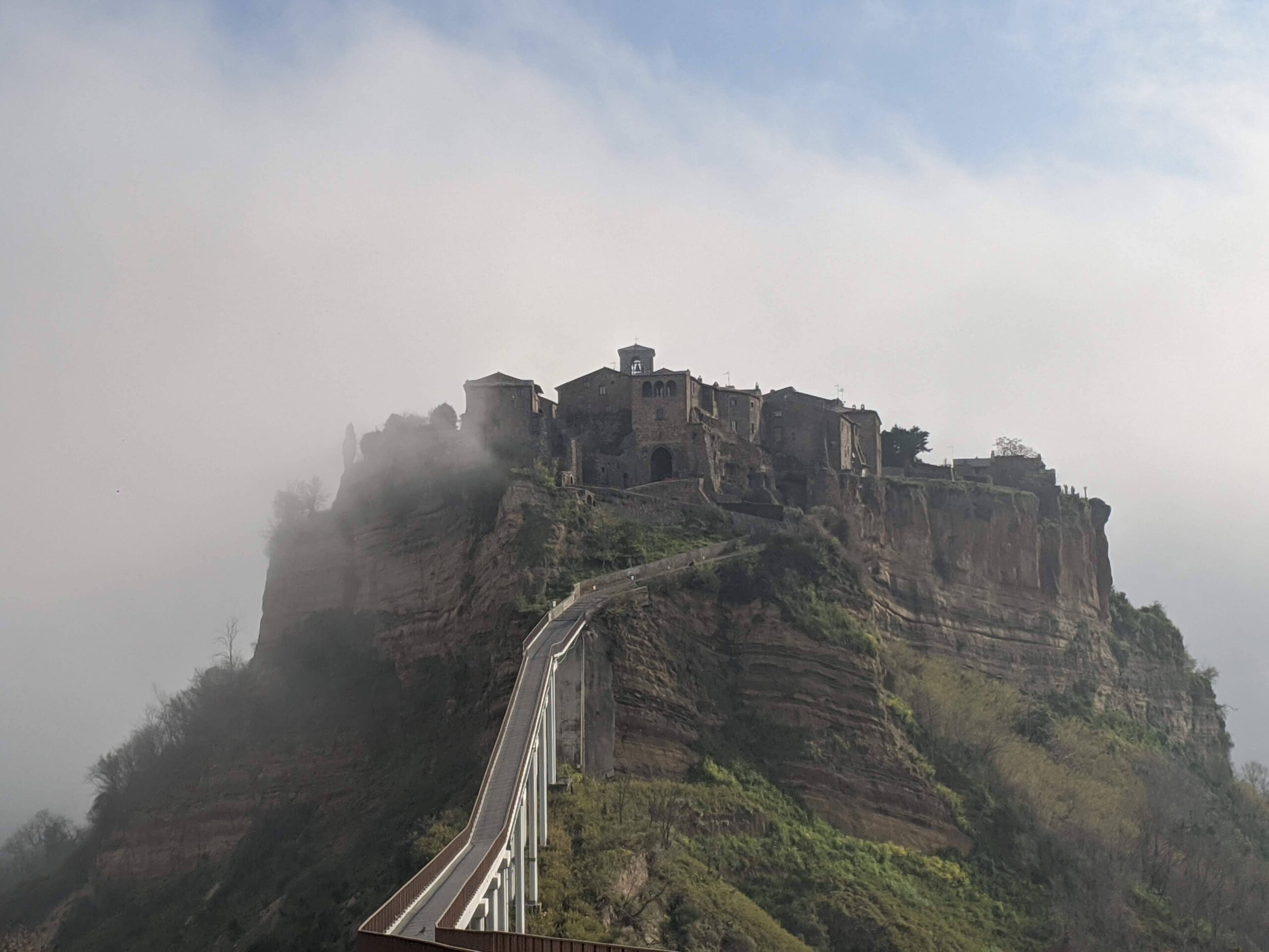 Cidade no alto da montanha, é possível ver suas casas em pedra escura e a ponte que leva até a cidade.