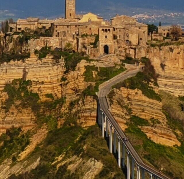 Foto de Civita di bagnoregio vista de longe, é possível ver suas casas no topo da montanha no estilo medieval, com uma ponte que leva até elas.