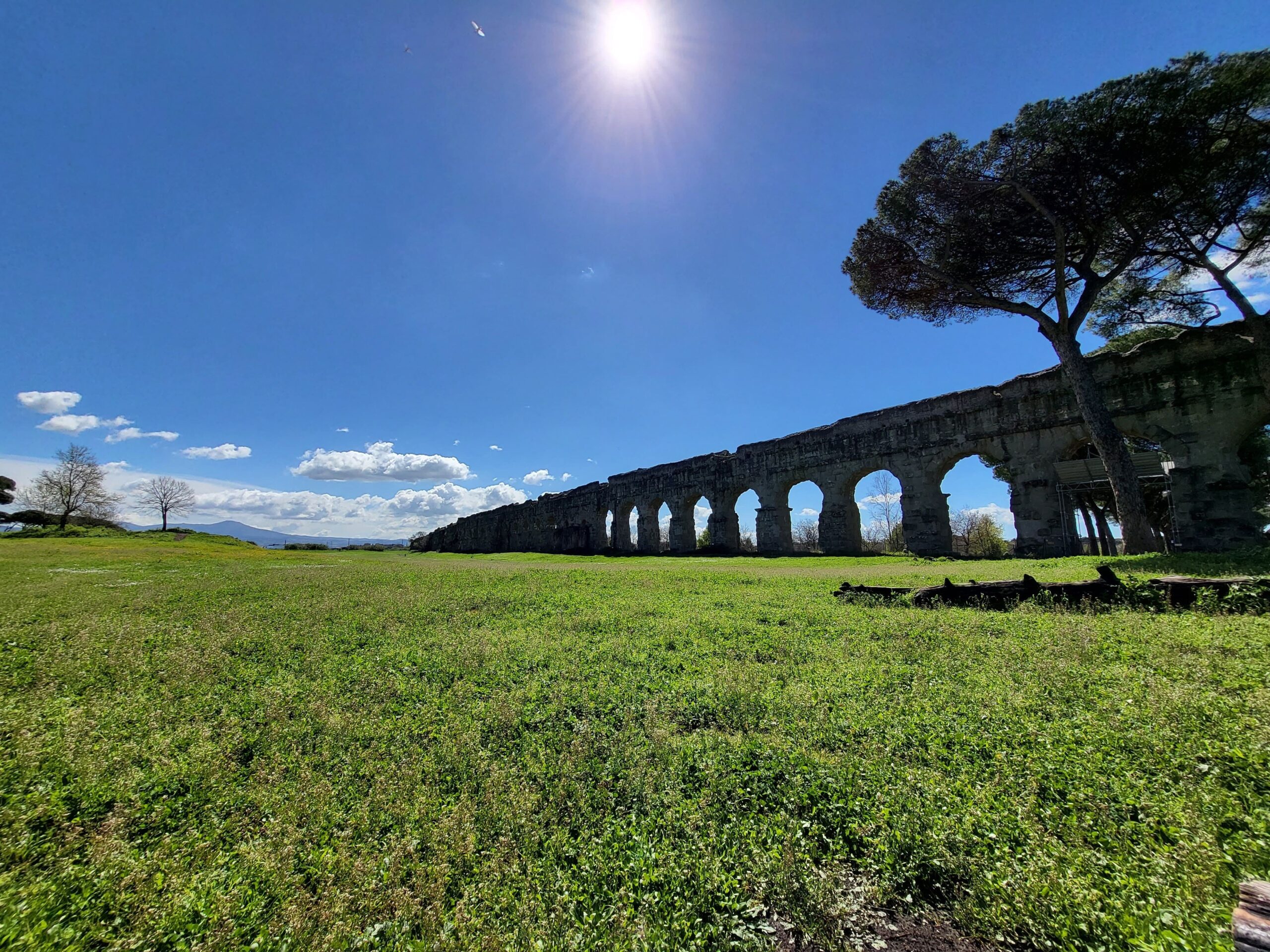 Foto de um grande aqueduto antigo em meio a um gramado verde.