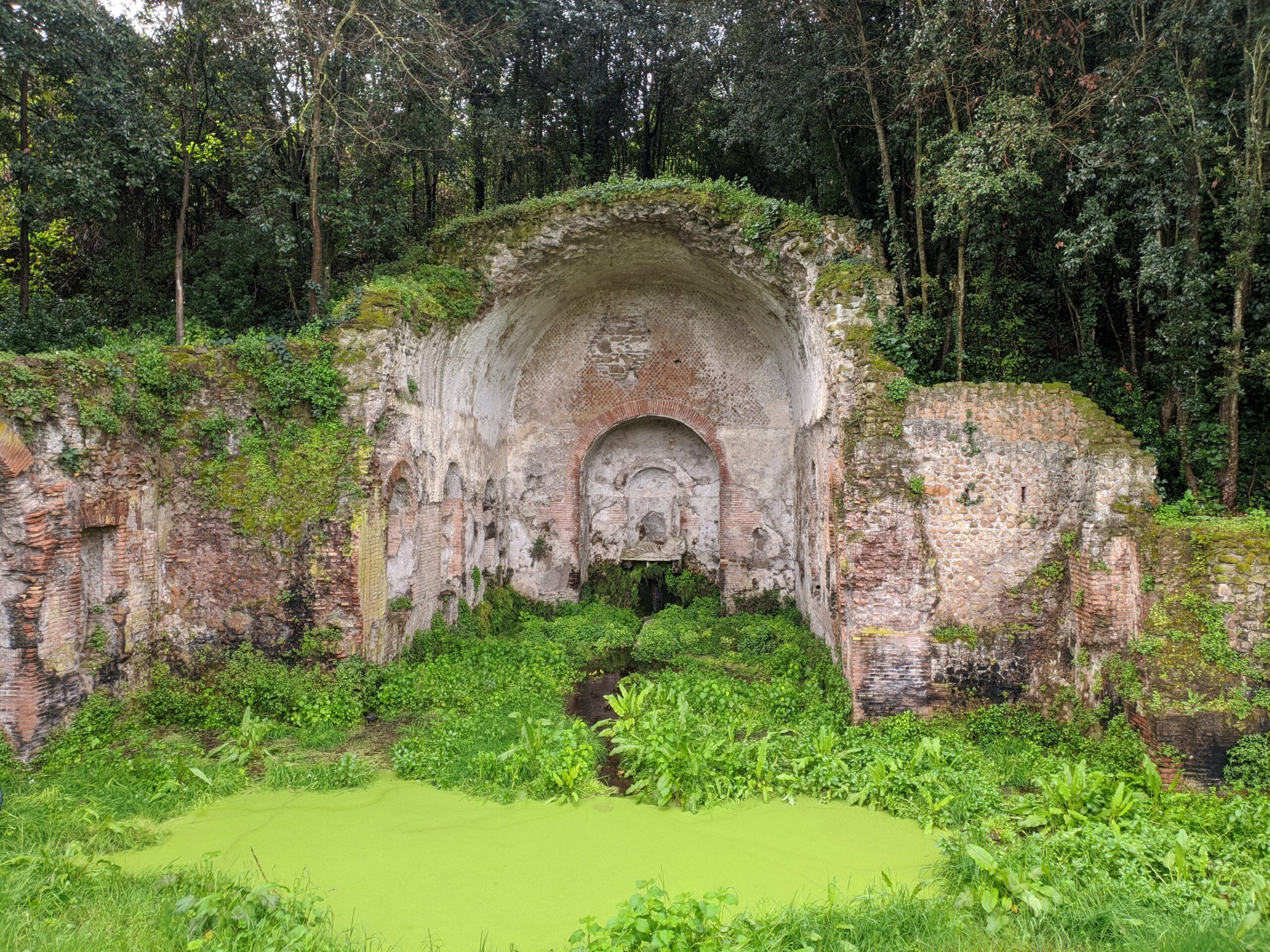 Foto de um templo antigo encravado em uma pedra, revelando uma antiga gruta e seus adornos. O seu solo lembra um pântano.