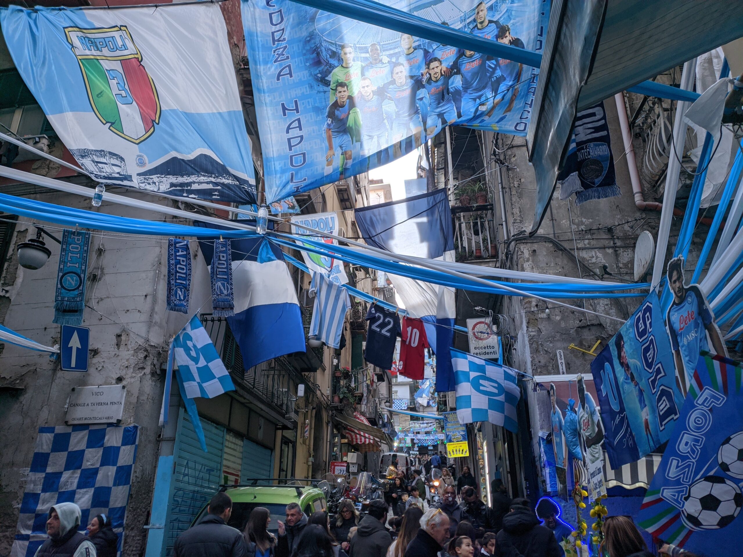 Uma rua com prédio antigos repleta de bandeiras e faixas nas cores azul e branca que cruzam de um prédio para outro.
