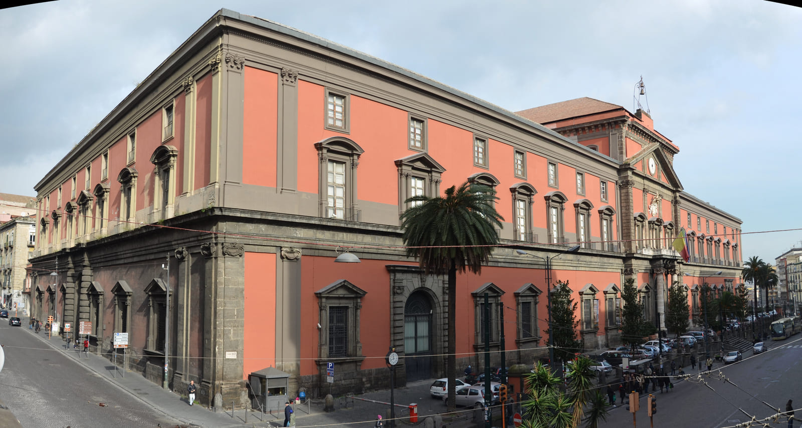 Foto da fachada de uma construção, o prédio lembra a arquitetura colonial, com grandes portas, sendo adornado por contornos de pedra sobre as janelas e em sua "moldura", o edifício é da cor laranja.