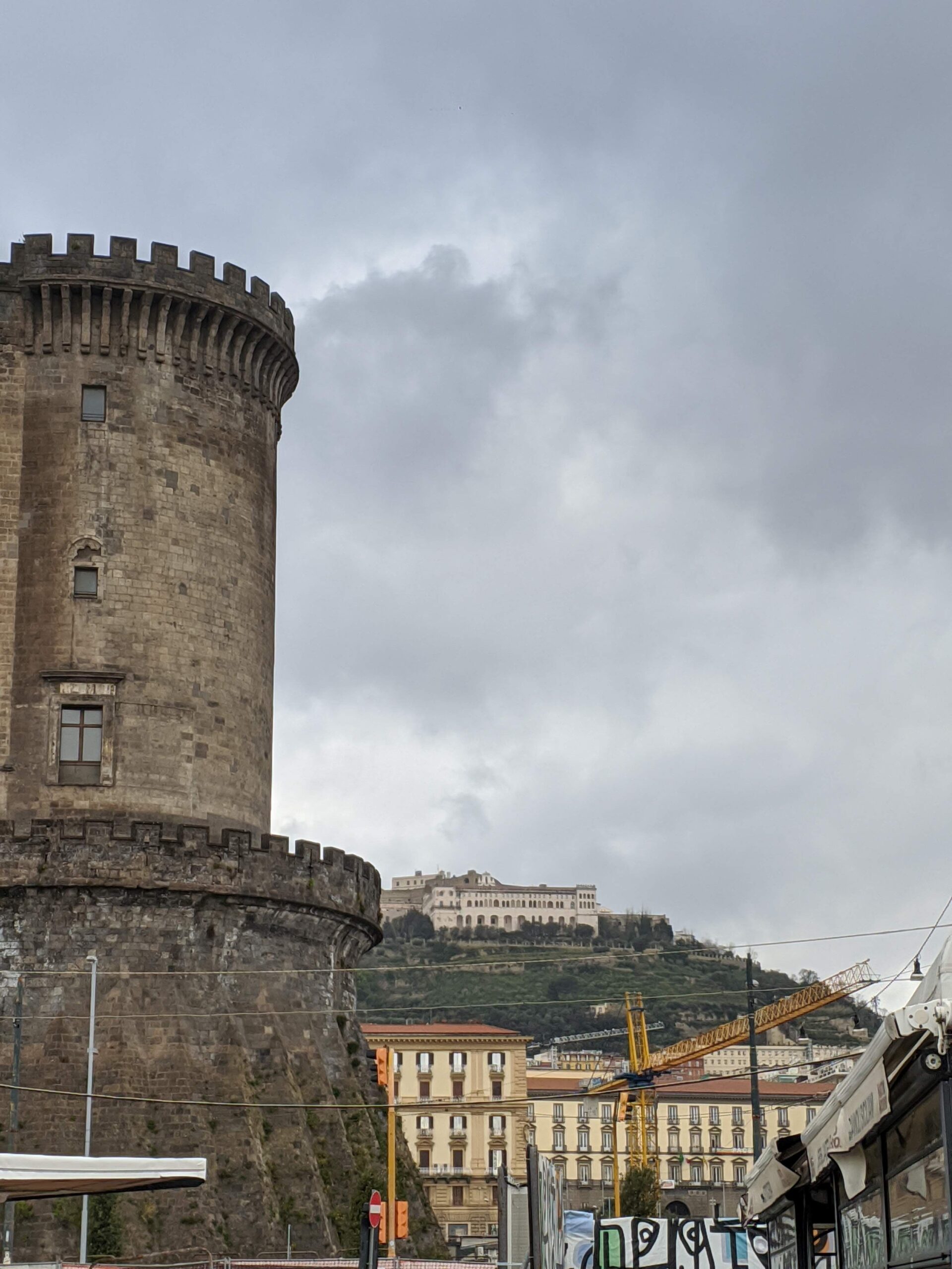 Foto da marulha de um castelo, em formato redondo e com o topo com pequenas aberturas na parede para observação. Ao fundo é possível ver uma montanha com outro castelo em seu topo.