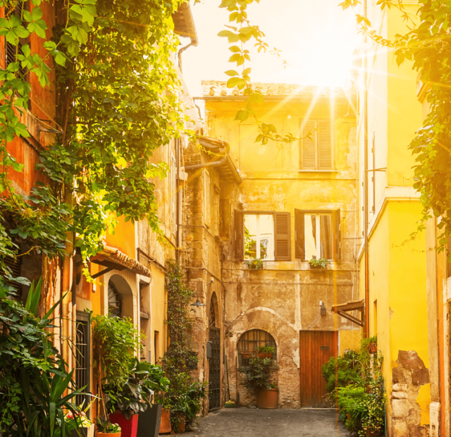 Uma ruela encantadora em Trastevere durante o dia, com o sol se pondo e banhando a cena em uma luz dourada, destacando a vegetação exuberante e a arquitetura tradicional com cores quentes