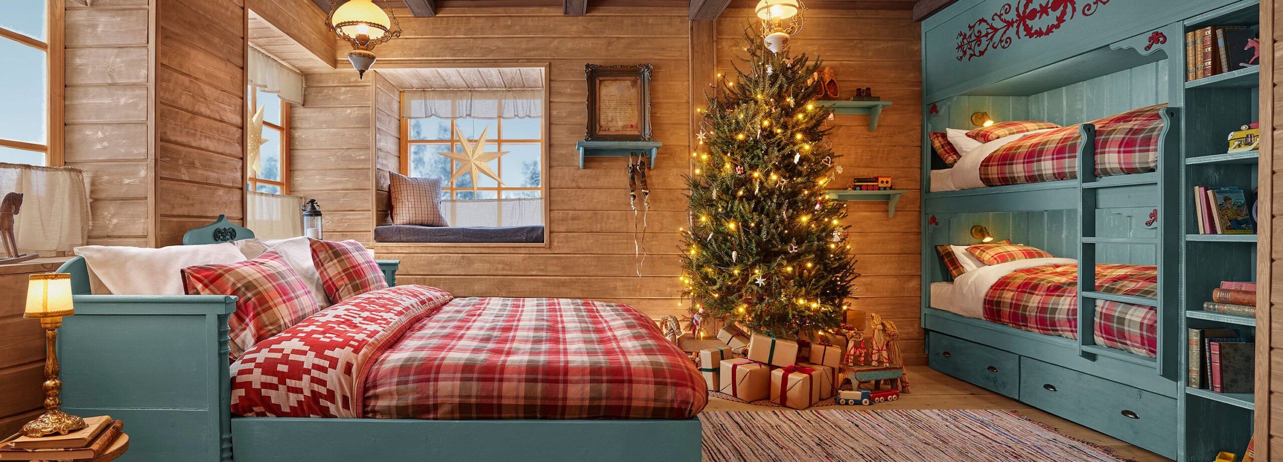 Quarto da Cabana do Papai Noel com cama de casal, árvore de Natal iluminada e beliches ao fundo em um ambiente rústico e festivo.