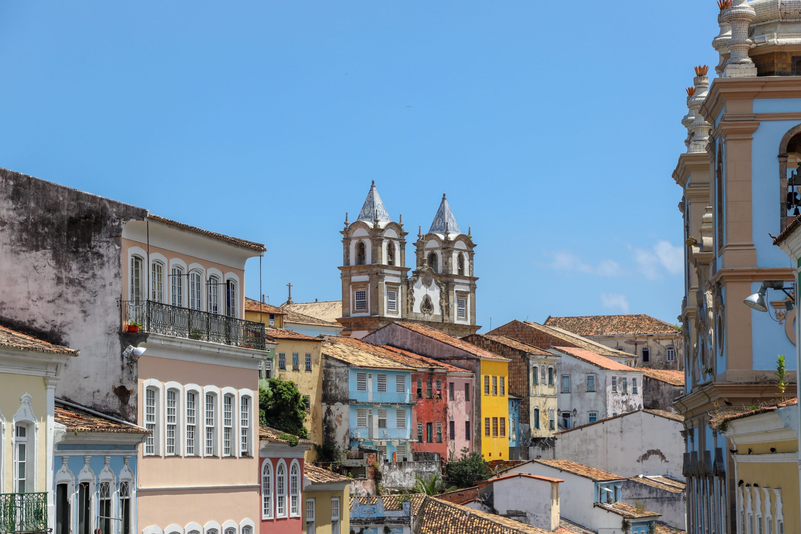 Cenário urbano colorido do centro histórico de Salvador com casas coloniais pintadas de cores vivas e igrejas barrocas destacando-se sob o céu azul claro