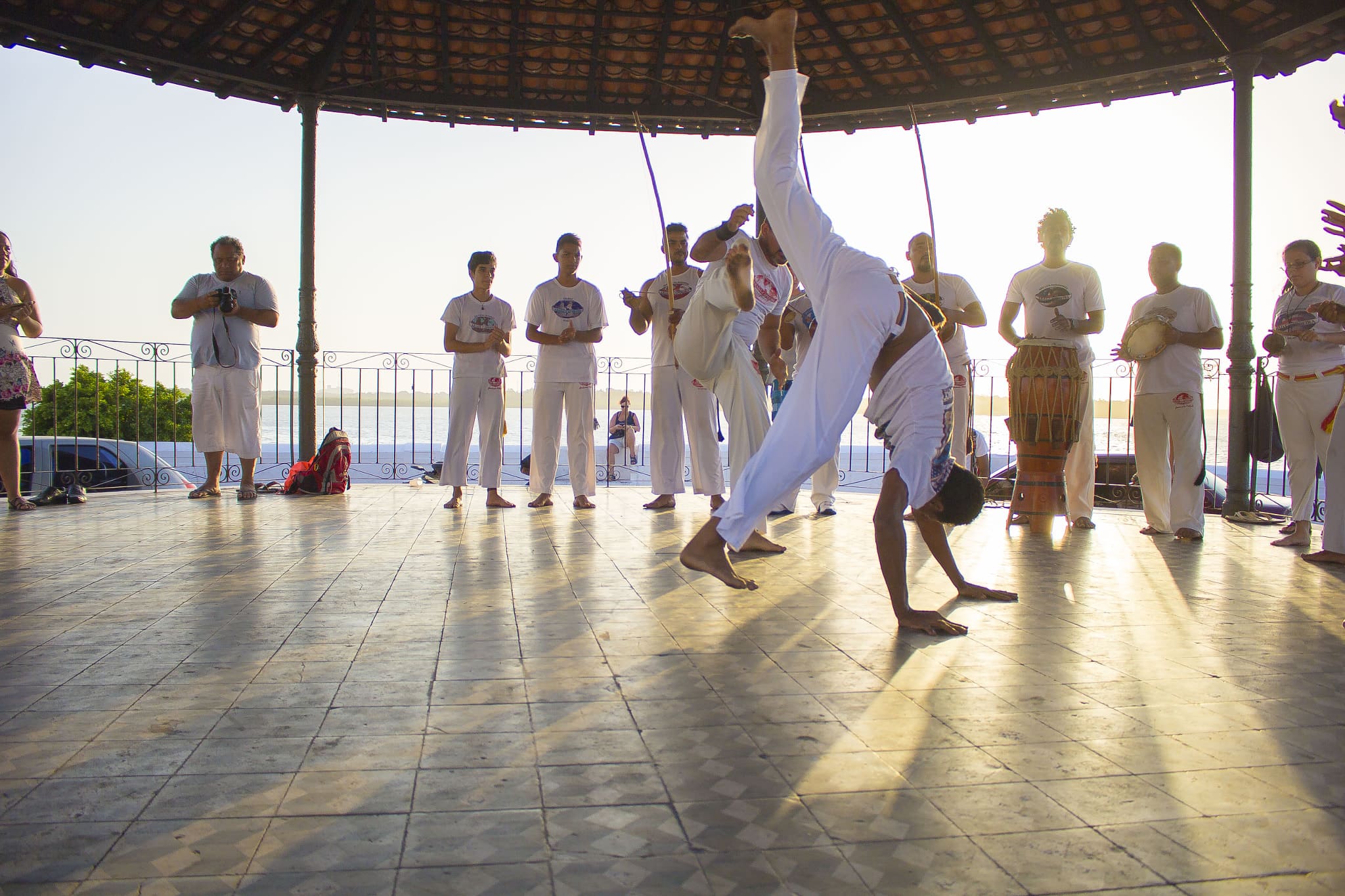 Roda de capoeira ao entardecer com praticantes em movimento e músicos tocando instrumentos tradicionais, celebrando esta arte afro-brasileira reconhecida como Patrimônio Imaterial da Humanidade pela UNESCO.