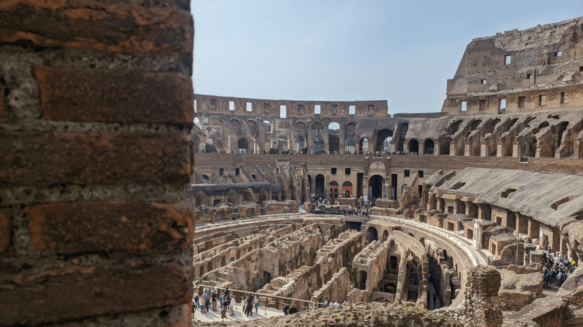 "Foto atual do interior do Coliseu, mostrando as ruínas, os arcos e os turistas explorando o local histórico.