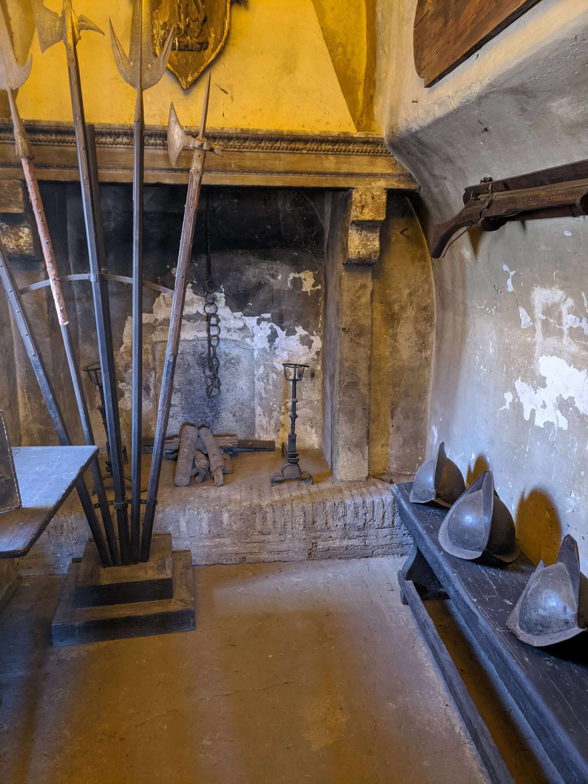 ala de armas dentro do Castelo Santo Ângelo com uma coleção de armas antigas, como lanças e armaduras, expostas ao lado de uma parede de pedra.