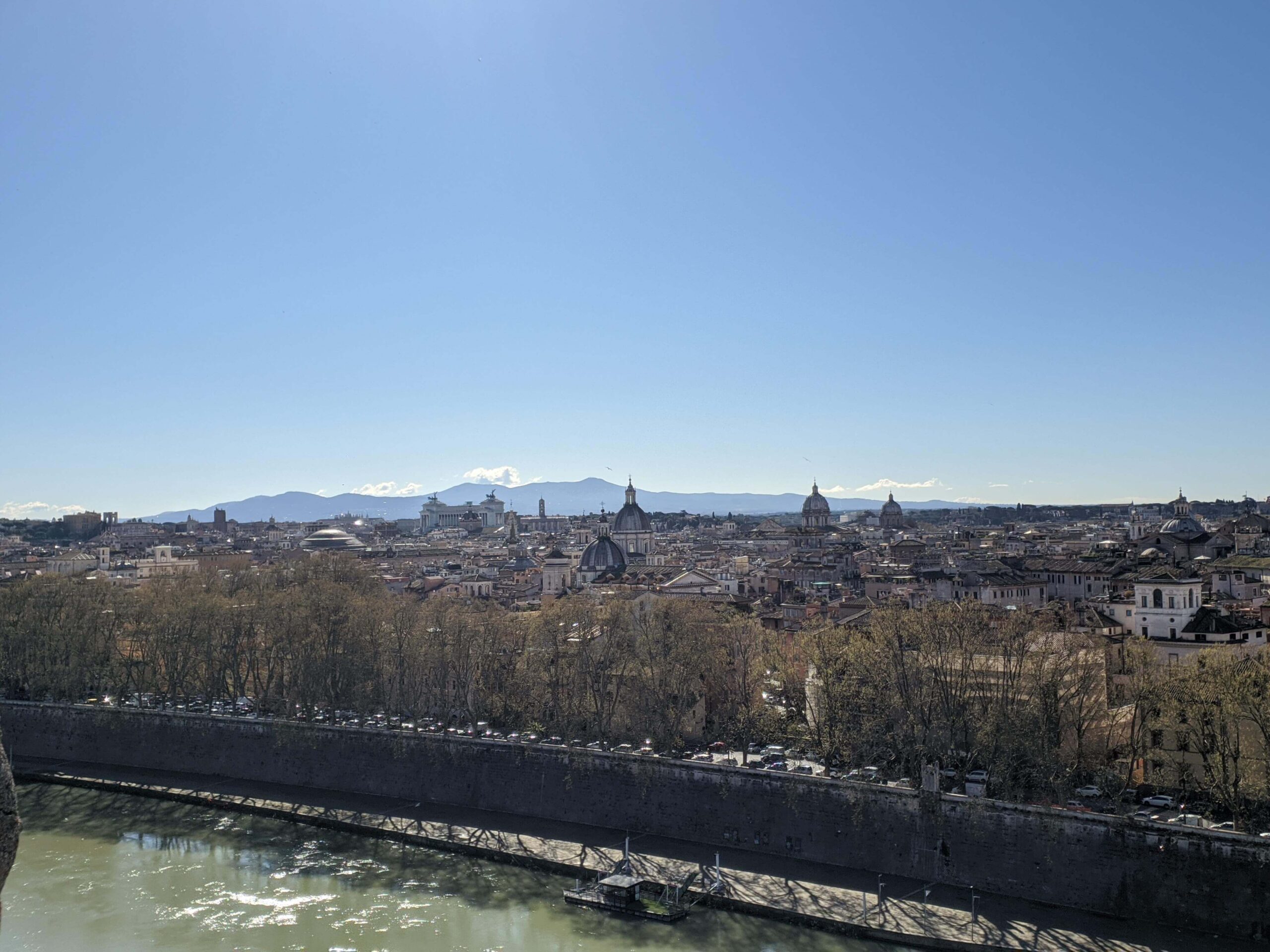 Paisagem urbana de Roma com o horizonte dominado por cúpulas e edifícios históricos, vista sob um céu azul claro.