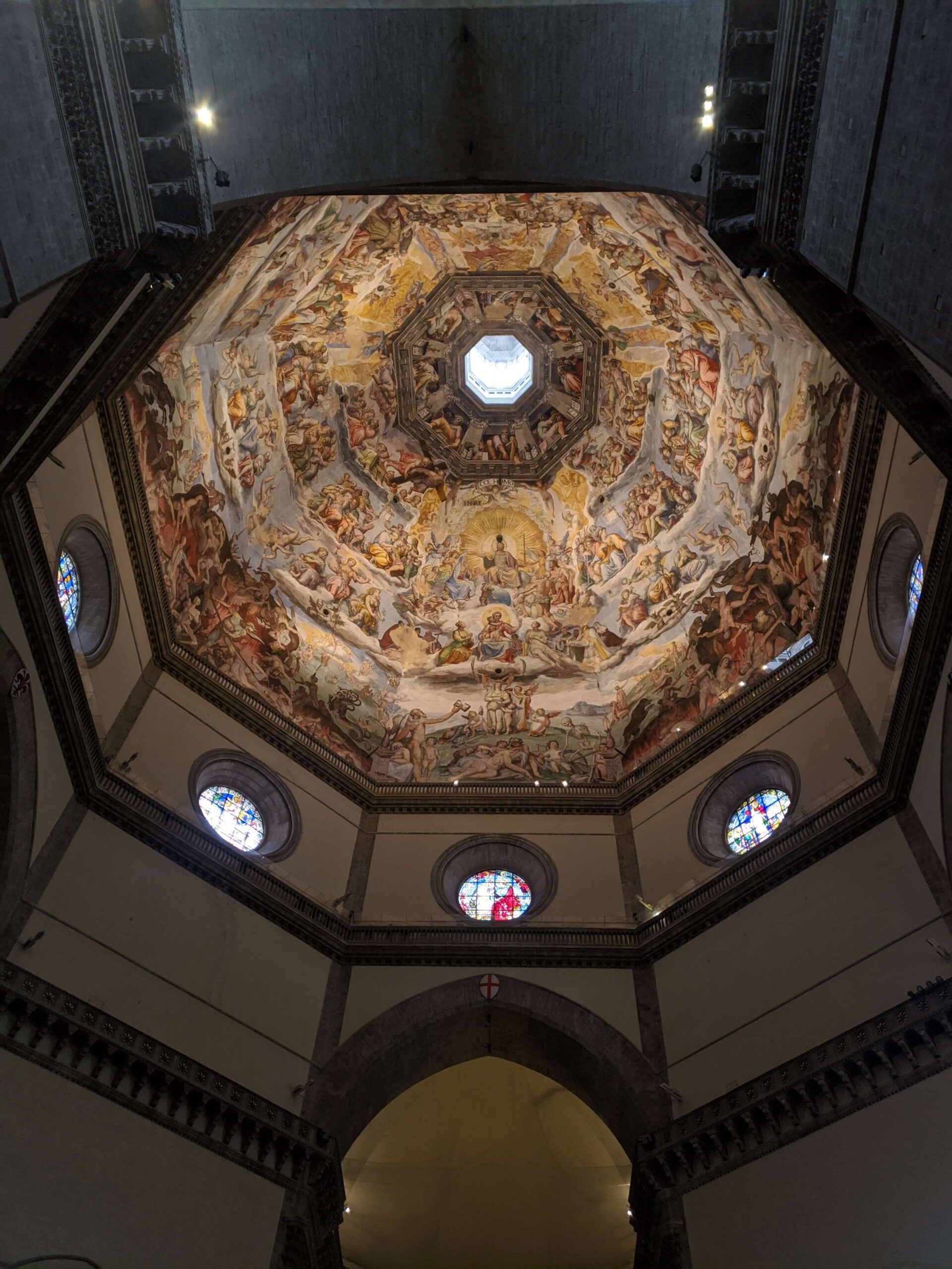 Imagem do interior da cúpula do Duomo de Florença, mostrando os afrescos vibrantes e detalhados que cobrem todo o teto, com a luz natural entrando pelo óculo central.