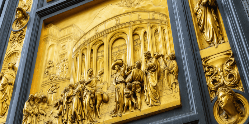 Painel dos famosos Painéis de Ghiberti, também conhecidos como Portas do Paraíso, do Batistério de Florença, mostrando um relevo dourado que representa cenas bíblicas com intrincados detalhes.