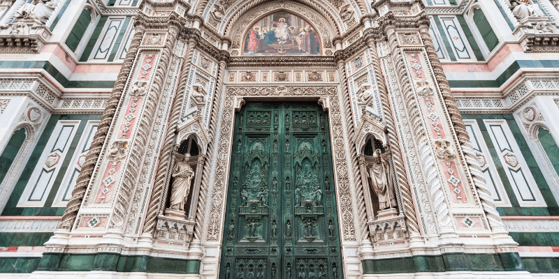 Porta da Mandorla do Duomo de Florença, uma entrada ricamente decorada com esculturas em relevo e detalhes arquitetônicos complexos, com uma grande porta de bronze no centro.